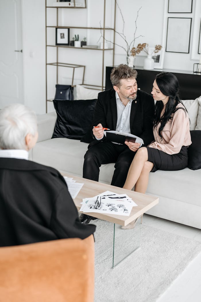 A mature couple sits with an advisor on a couch, discussing documents in a modern office.