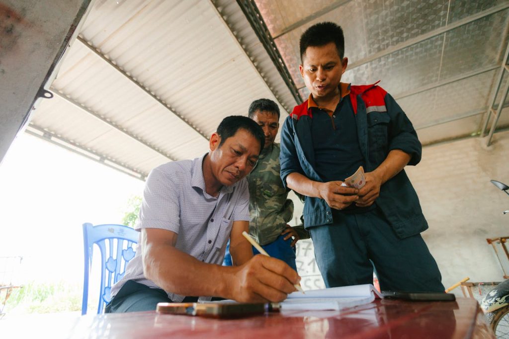 Three men involved in a financial transaction, with one signing documents indoors.