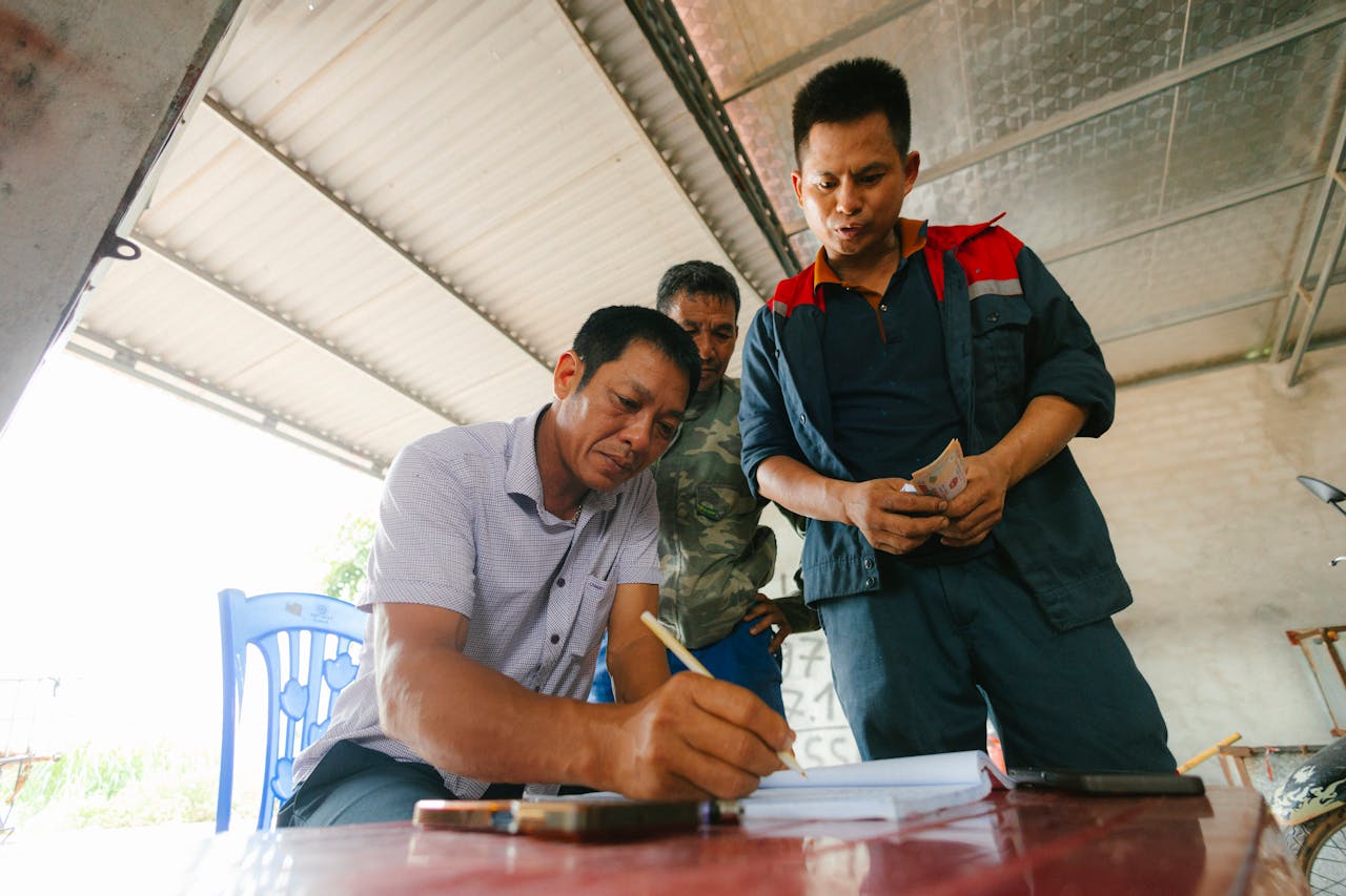Three men involved in a financial transaction, with one signing documents indoors.